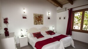 A double bed with two red pillows, a white bedside table, a wall-mounted lamp, and a window with a view of greenery. - Son Mulet - Beautiful villa with private pool and garden in Llubí (Llubí)
