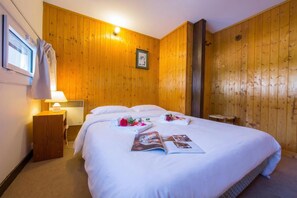 A hotel room with wooden walls, a bed with white linens, a bedside table with a lamp, and a framed picture on the wall. - Grand Roc C114 280m from Slopes, View, Parking & WiFi, Argentière (Chamonix), France (Argentière (Chamonix))