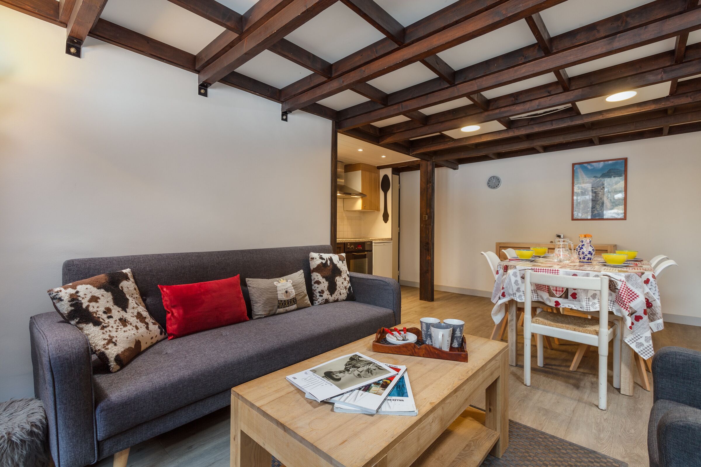 Sala de estar com sofá cinza, mesa de centro de madeira e área de jantar com mesa posta para dois.