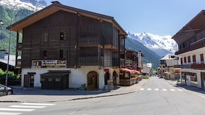A wooden building with a café sign, a street with crosswalks, and snow-capped mountains in the background.