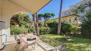 Eine Terrasse im Freien mit Esstisch, umgeben von einem Garten und Blick auf Wohnhäuser.
