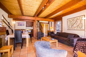 Een ruime woonkamer met een houten plafond, een eettafel met stoelen, een bank en een salontafel.