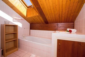 Un baño con tragaluz, bañera, repisa de madera y tocador con una toalla y una rosa.