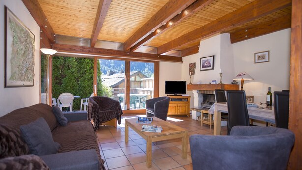 Ein geräumiger Wohnbereich mit Holzboden, einer Couch, einem Couchtisch, einem Fernseher und einem Esstisch mit Stühlen.