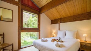 Ein Schlafzimmer mit einem großen Bett, zwei Nachttischen mit Lampen, einem Sessel und einem Fenster mit Blick auf Grünflächen.