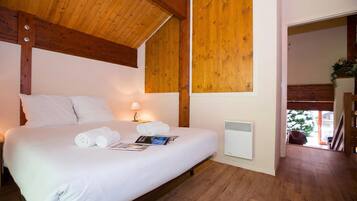 Een slaapkamer met een houten plafond, een bed met witte beddengoed, een nachtkastje met een lamp en een radiator.