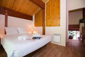 Une chambre avec un plafond en bois, un lit avec une literie blanche, une table de chevet avec une lampe et un radiateur.