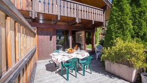 Eine Holzterrasse mit Esstisch, umgeben von viel Grün.