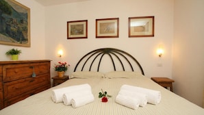 Una cama bien hecha con ropa de cama a rayas, dos mesitas de noche con lámparas, un aparador de madera y tres cuadros en la pared.