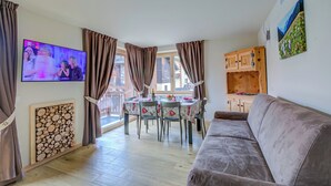 Een woonkamer met een televisie, een eettafel, stoelen, een bank en een houten kast.