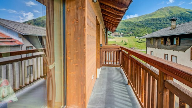 Een balkon met houten spijlen, uitzicht op een berg en een gebouw met een schuin dak.