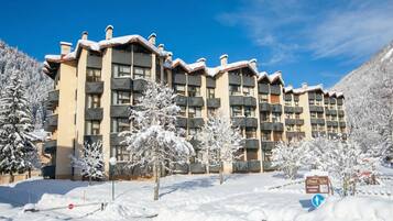 Un hôtel à plusieurs étages doté de balcons, entouré d’arbres couverts de neige et surplombant un ciel dégagé.