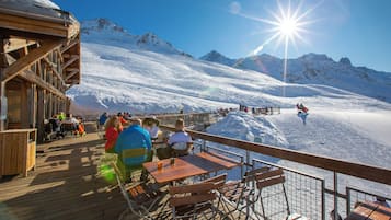 Une terrasse en bois, agrémentée de tables et de chaises, qui offre une vue sur un paysage montagneux enneigé.