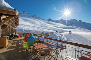 Eine Holzterrasse mit Tischen und Stühlen mit Blick auf eine verschneite Berglandschaft.