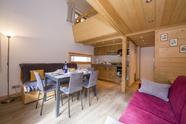 A cozy living room with a dining area, wooden ceiling, and a kitchenette.