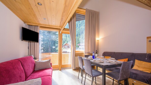 A modern interior with a red sofa, a dining table with chairs, a flat-screen TV mounted on the wall, and large windows offering a view of the outdoors. - Grand Roc B121 260m from Slopes, View & Parking, Argentière (Chamonix), France (Argentière (Chamonix))