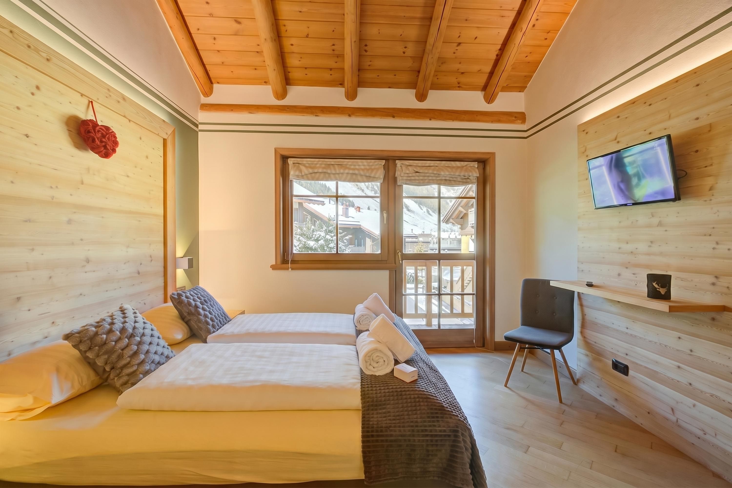 A hotel room with two beds, a TV, a chair, and a window with a view of a snowy landscape.