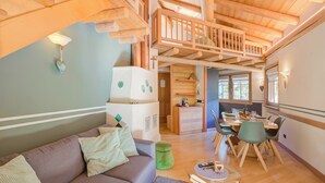 A cozy living room with a sofa, a dining table with chairs, a kitchen area, and a loft space with a wooden staircase. - Bucaneve, Livigno, Italy (Livigno)