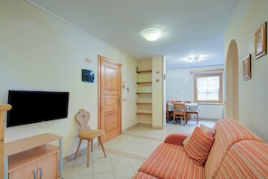 Una sala de estar con televisor, sofá, puerta de madera y un comedor con mesa y sillas.