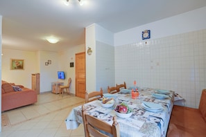 Un comedor con una mesa dispuesta para cuatro personas, rodeada de sillas de madera. Se ve un televisor montado en la pared y una puerta de madera al fondo.