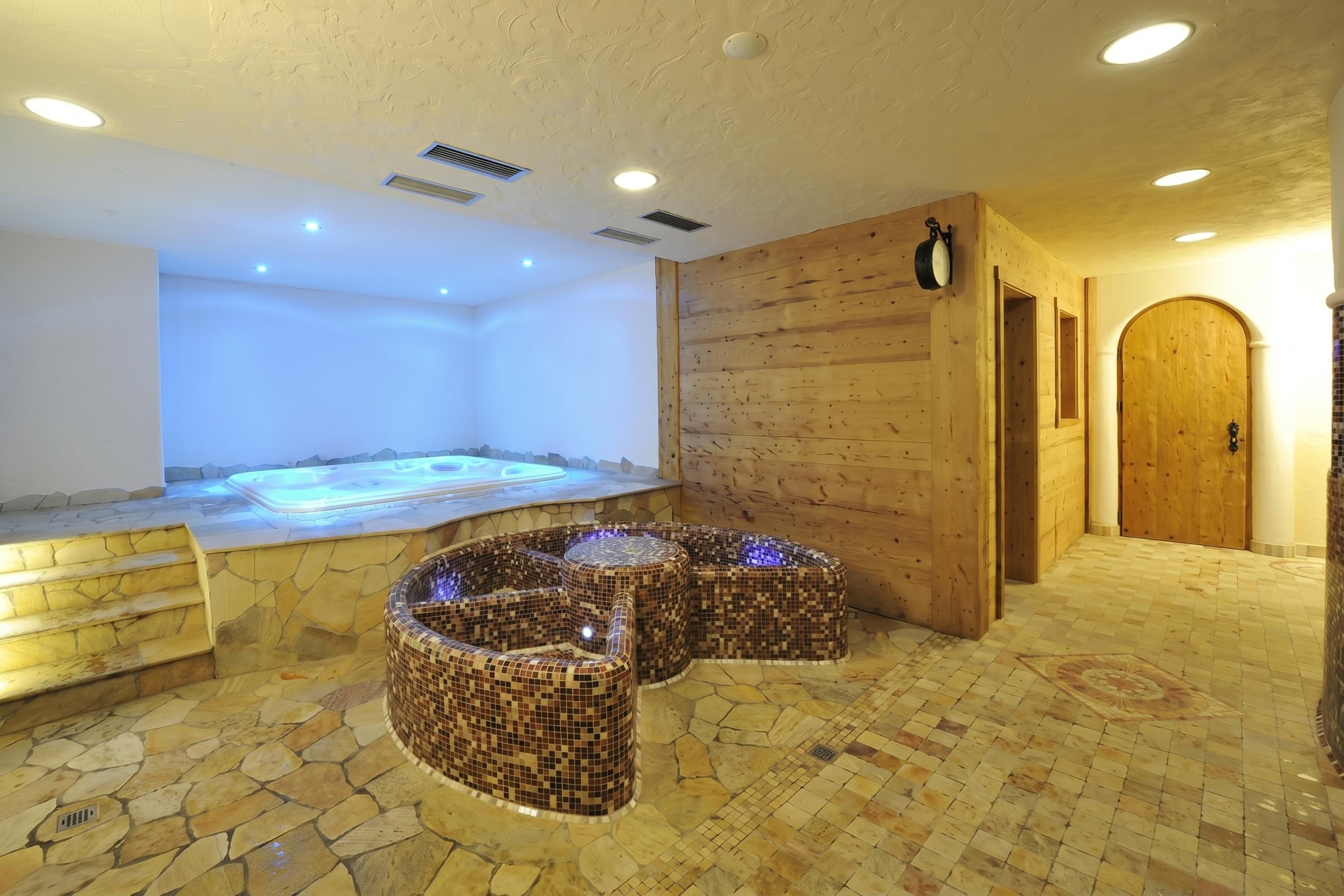 A spa area with a hot tub, mosaic seating, stone flooring, wooden walls, and a wooden door.