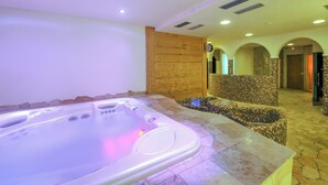 A spa area with a hot tub, stone flooring, and a wooden wall. - Stella Alpina, Livigno, Italy (Livigno)