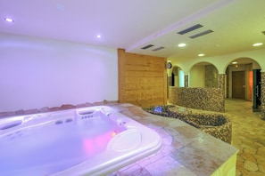 Zona de spa con jacuzzi, suelo de piedra y puertas de arco.