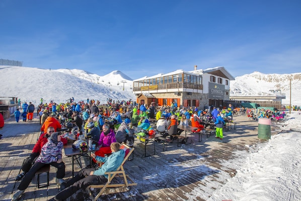 A crowded outdoor seating area with tables and chairs, a building with a balcony, and a snowy mountain backdrop. - Stella Alpina, Livigno, Italy (Livigno)