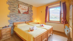 A double room with two beds, a stone wall, a window with a view, and a wooden chair. - Stella Alpina, Livigno, Italy (Livigno)