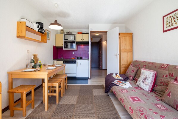 A compact living space with a kitchenette, dining area, and a sofa with patterned cushions.
