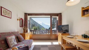 A cozy room with a sofa, a dining table, a TV, and a view of mountains. - La Verte 12 Ski In/Ski Out | Grands Montets | Argentière Chamonix, Argentière (Chamonix), France (Argentière (Chamonix))