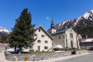Une église à la façade en pierre, dotée d’un clocher, avec une montagne enneigée en arrière-plan.
