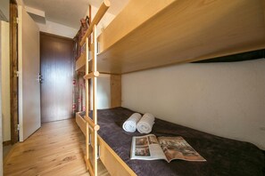 A bunk bed with a wooden frame, a dark mattress, and two rolled towels.