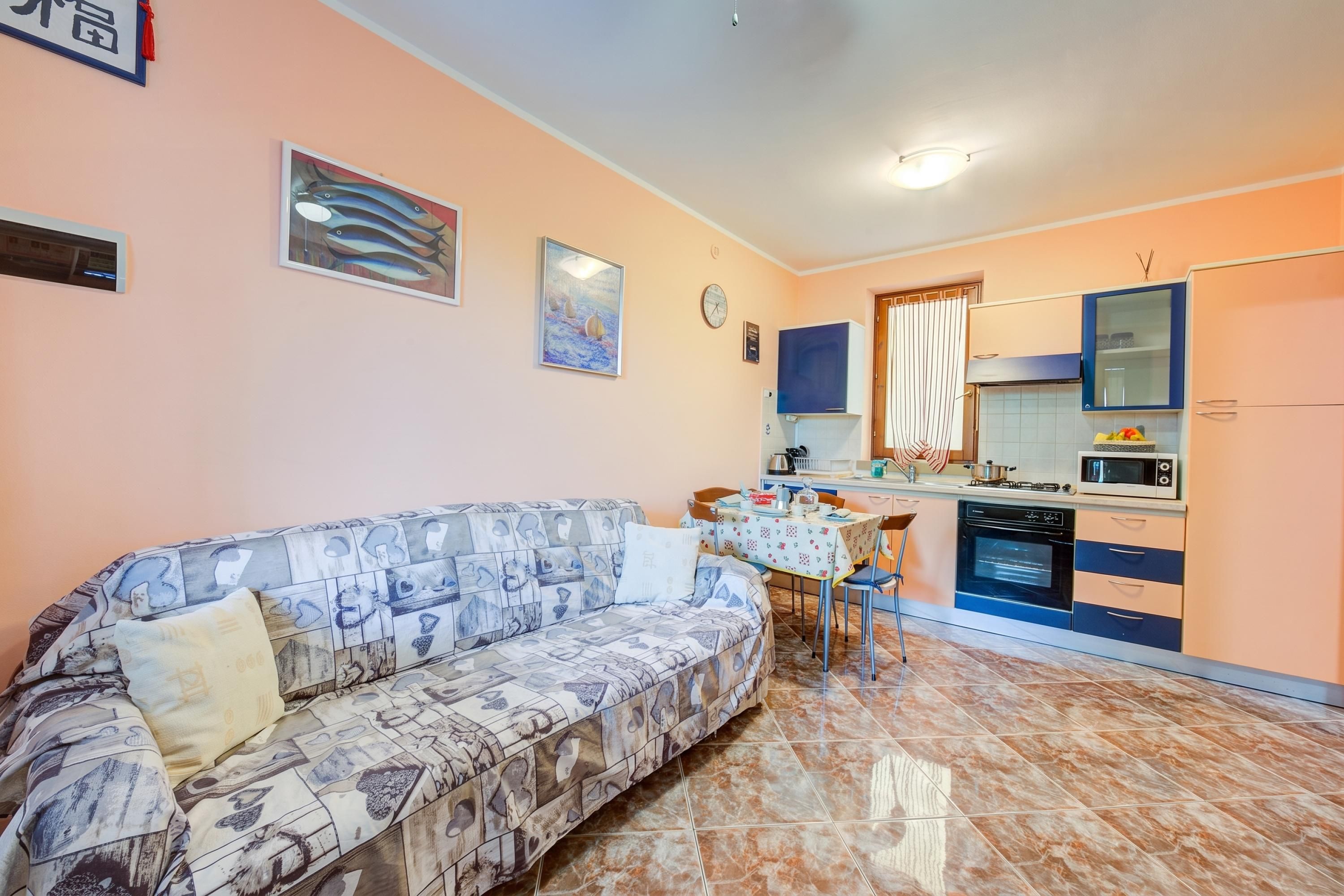 A compact living space with a sofa, dining table, kitchen area, and a clock on the wall.