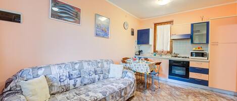 A compact living space with a sofa, dining table, kitchen area, and a clock on the wall.
