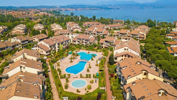 Zona residencial con edificios de apartamentos, una piscina central y un lago al fondo.
