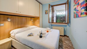Habitación de hotel con cama, mesita de noche, ventana con vistas y un cuadro abstracto colorido en la pared.