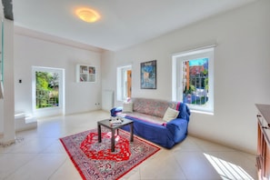 A spacious living room with a blue sofa, a red patterned rug, and a bookshelf.