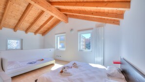Un dormitorio con techo de madera inclinado, dos camas y dos ventanas.
