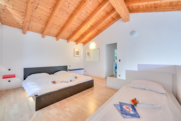 A modern bedroom with a wooden ceiling, a large bed, a smaller bed, and a bedside table with a book and a flower.