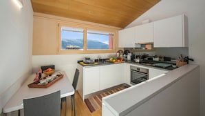 A modern kitchen with white cabinets, a wooden ceiling, and a large window offering a view of the mountains. - Ca' Melin with Balcony & Fireplace, Vezio, Switzerland (Vezio)