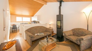 A living room with two sofas, a glass coffee table, a fireplace, and a kitchen in the background. - Ca' Melin with Balcony & Fireplace, Vezio, Switzerland (Vezio)