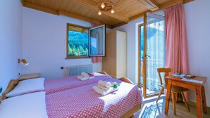 A bedroom with two beds, a wooden ceiling, a window with a view, a table with chairs, and a radiator. - Cervo Ski in - Ski out 200m, Livigno, Italy (Livigno)