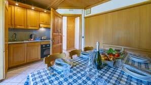A kitchen with wooden cabinets, a stove, and a dining table set for four with plates, glasses, and a bottle. - Cervo Ski in - Ski out 200m, Livigno, Italy (Livigno)
