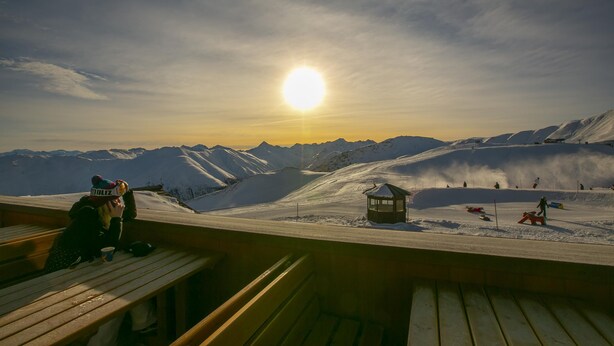 A wooden bench overlooking a snowy mountain landscape with a sun setting in the background. - Cervo Ski in - Ski out 200m, Livigno, Italy (Livigno)