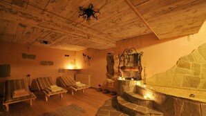 A room with a stone fireplace, wooden ceiling, and striped lounge chairs. - Rubino Ski in, Livigno, Italy (Livigno)