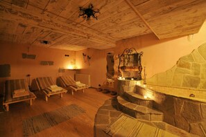 Ein Zimmer mit Holzdielen, einem Steinkamin und gestreiften Lounge-Sesseln.