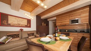A dining area with a wooden table, chairs, a sofa, a kitchen with a microwave, and a framed picture on the wall. - Rubino Ski in, Livigno, Italy (Livigno)