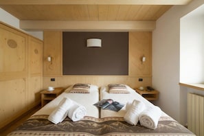 Ein Hotelzimmer mit Holzboden, zwei Betten mit Bettwäsche mit Bergmuster, Nachttischen mit Lampen und einem großen Fenster.