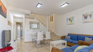 A modern living room with a blue sofa, white chairs, a TV, and a staircase leading to another level. - Fantastic Duplex in Puerto Rico (Mogán)